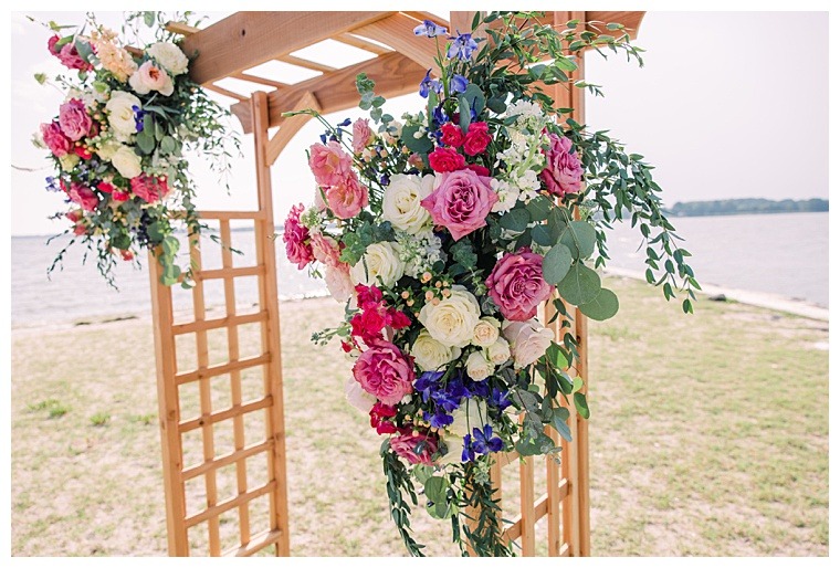Florals detail the natural bamboo archway at Tred Avon Yacht Club for a colorful waterfront ceremony